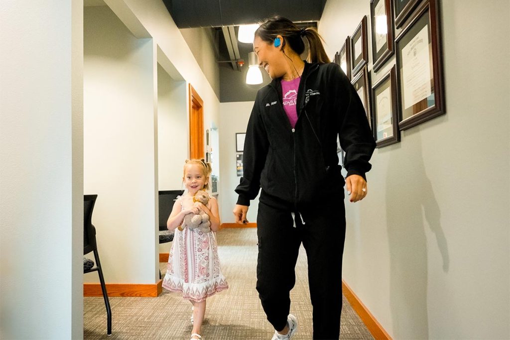 a child walks with dental hygienist Ali down a hallway at Great Plains Dental in Sioux Falls, SD
